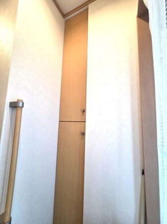 玄関には縦長の収納スペースが設けられておりすっきりとしたデザインです。木目調の扉が温かみのある印象を与えます。手すりも設置されていて出入りの際に安心です。コンパクトな空間ながらも機能性を感じられます。 玄関