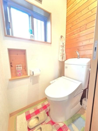 木の温もりを感じる壁面が印象的なトイレです。明るい窓からの自然光が空間を爽やかに照らします。収納スペースも確保されており実用性も備えています。シンプルながらも清潔感のある空間です。 トイレ